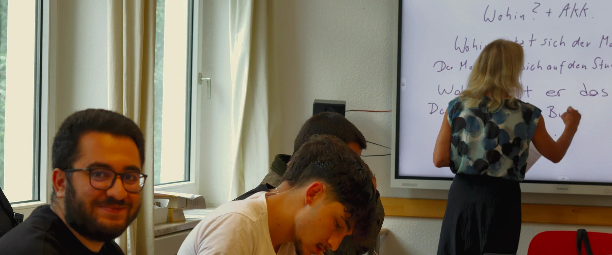 Teilnehmende schreiben, die Lehrerin schreibt Grammatik an die Tafel