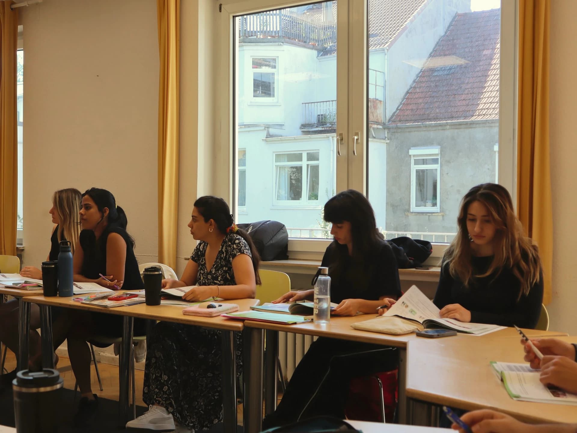 Teilnehmerinnen an einem langen Tisch am Fenster folgen dem Deutschunterricht